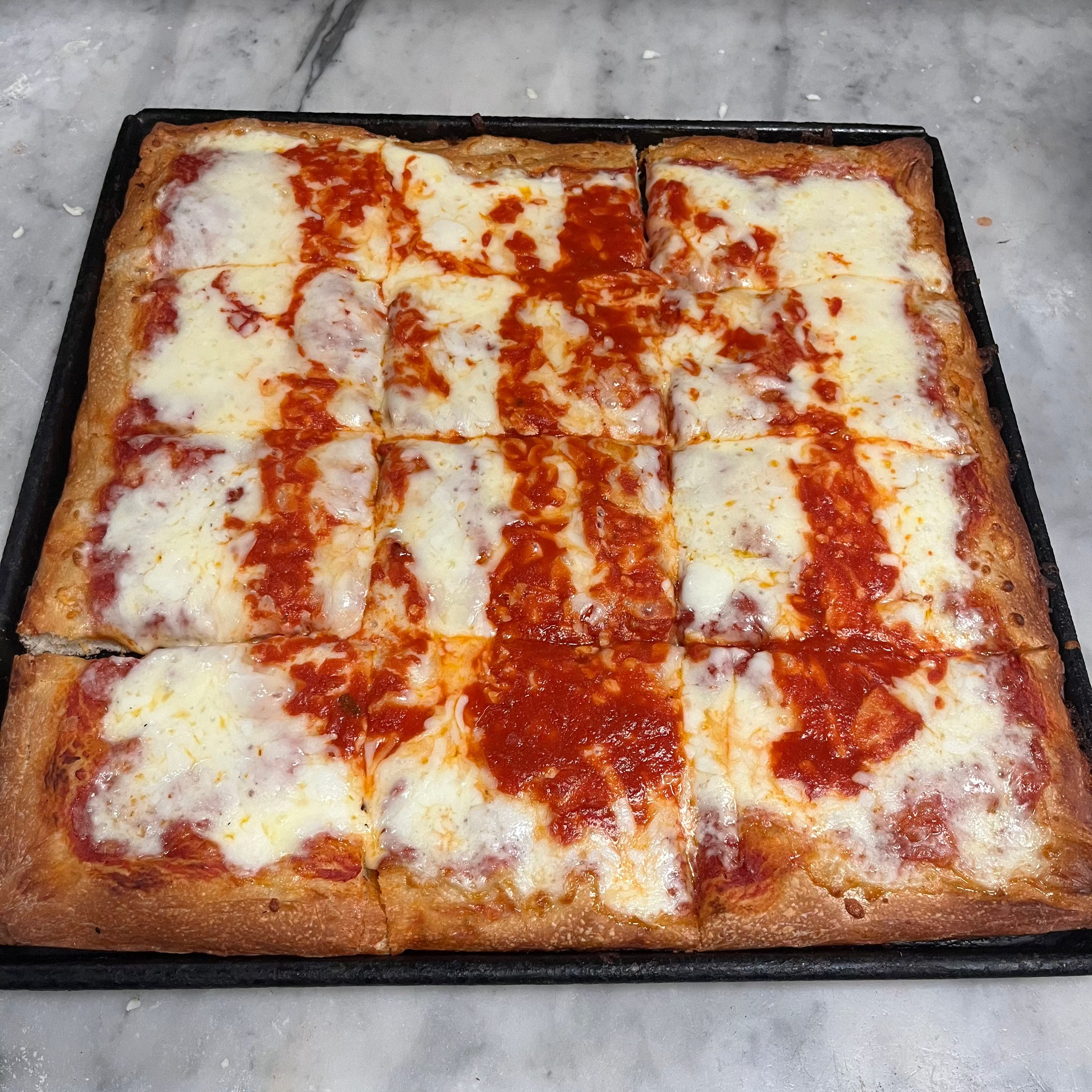 Square pizza with tomato sauce and cheese on a baking tray.